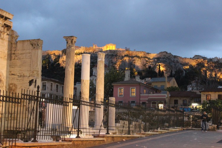 Pelas ruas de Atenas com a visão noturna da Acrópoles, no alto.